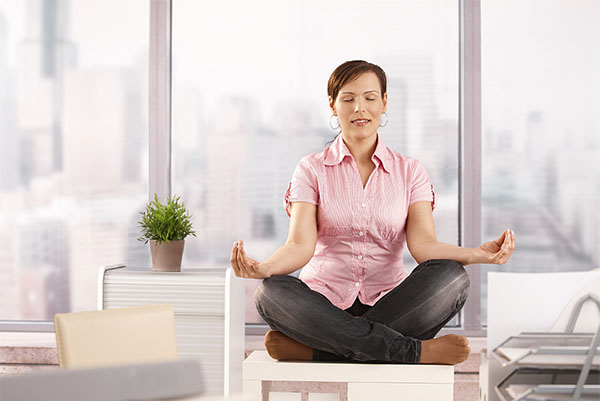 Relaxed office worker sitting on cabinet, doing yoga meditation with closed eyes, smiling.