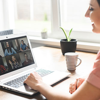 Communication on distance via video, video call, zoom. A young attractive woman using app on laptop for meeting with friends. She looks at webcam and smiles. Side view